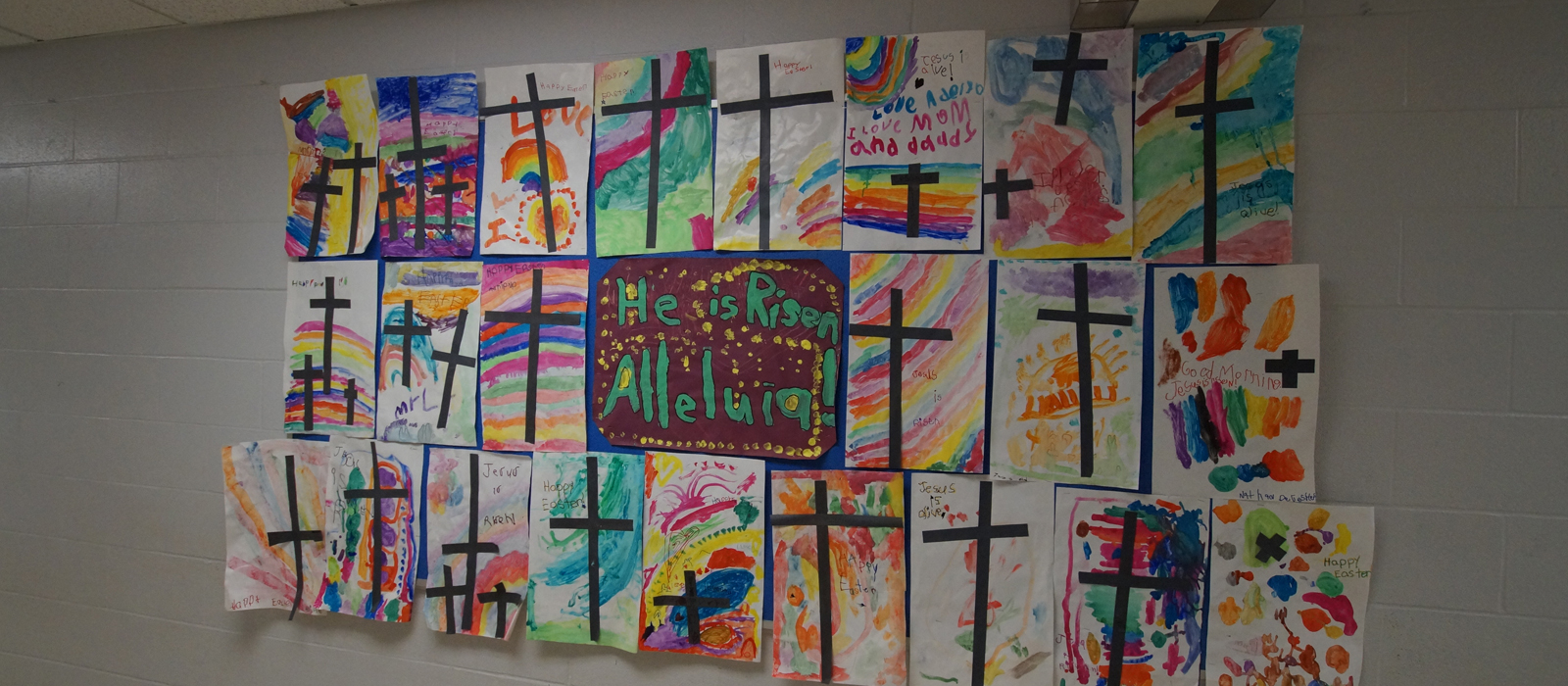 Decorative paintings with crosses and rainbow colours with "He is Risen, Alleluia!" painted in the middle.