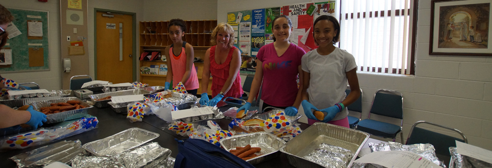 Volunteer with three students during hot dog day.